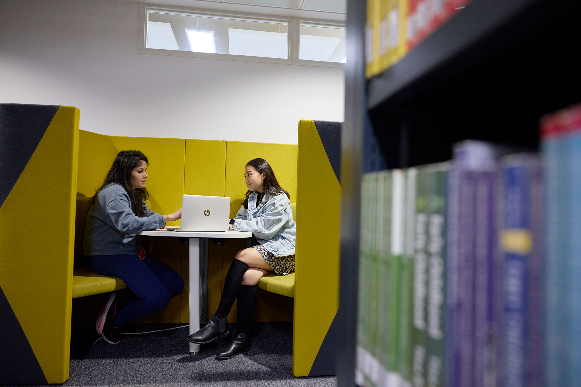 Two students sitting with a laptop is a secluded chair area of the library.