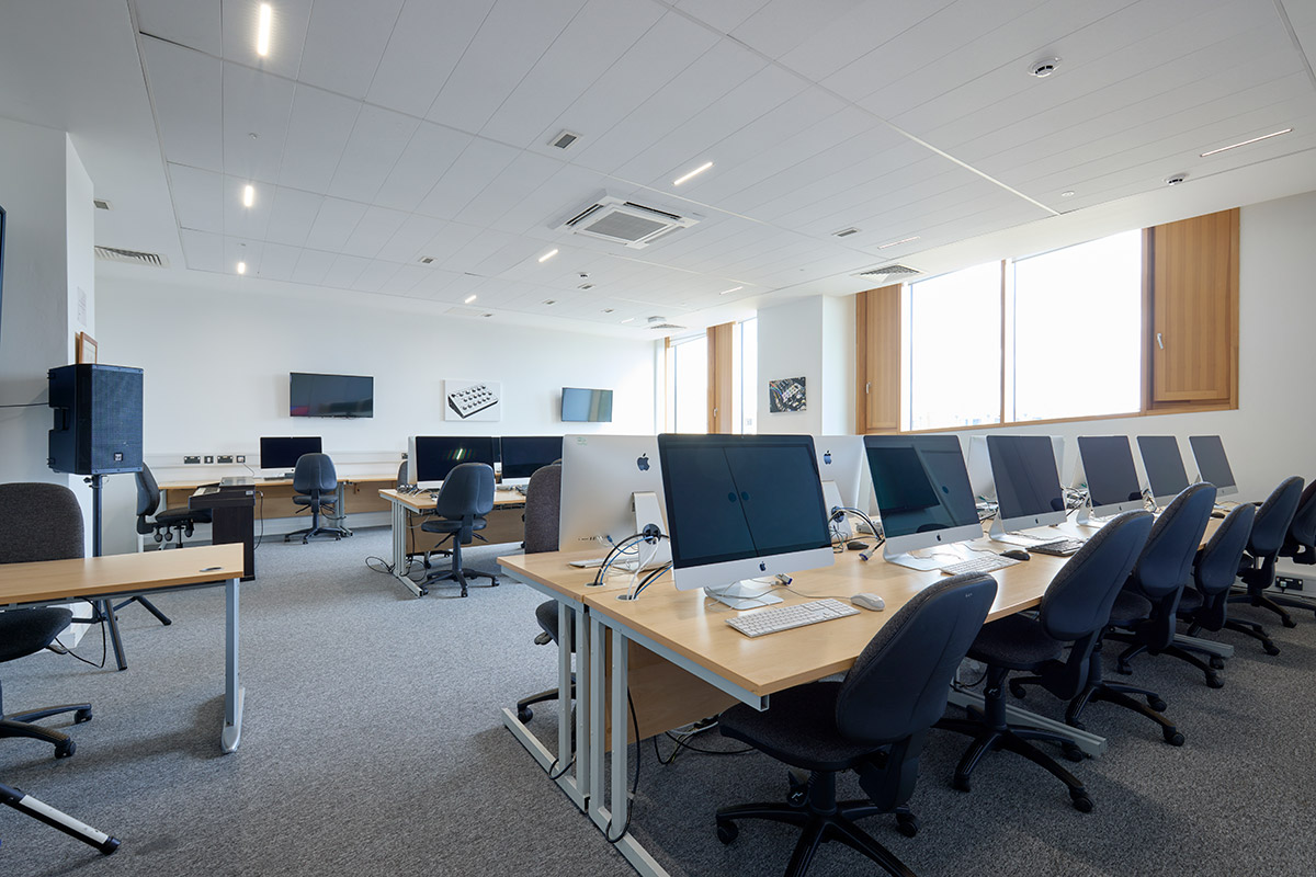 Internal view of Mac Suite, showing 2 desk stations with 12 per station, with other computers and screens around the room.