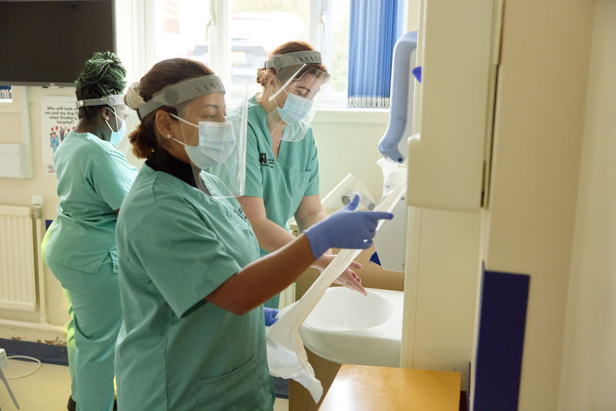 Group of dental nursing students wearing scrubs and face masks. They are washing hands and taking tissue, preparing for a practice session. They are in the Dental Nursing Simulation space at NGH