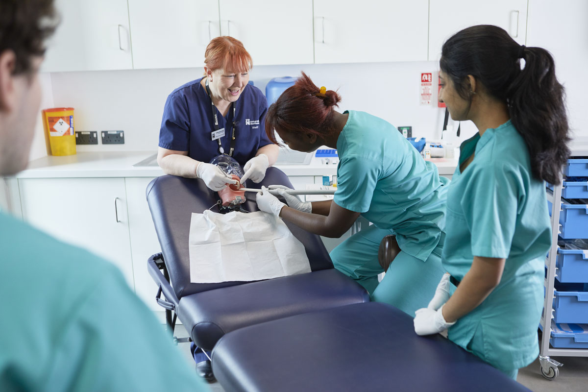 A group of dental nurses working on a manikin patient's mouth with a suction tool, in the UON dental nursing labs