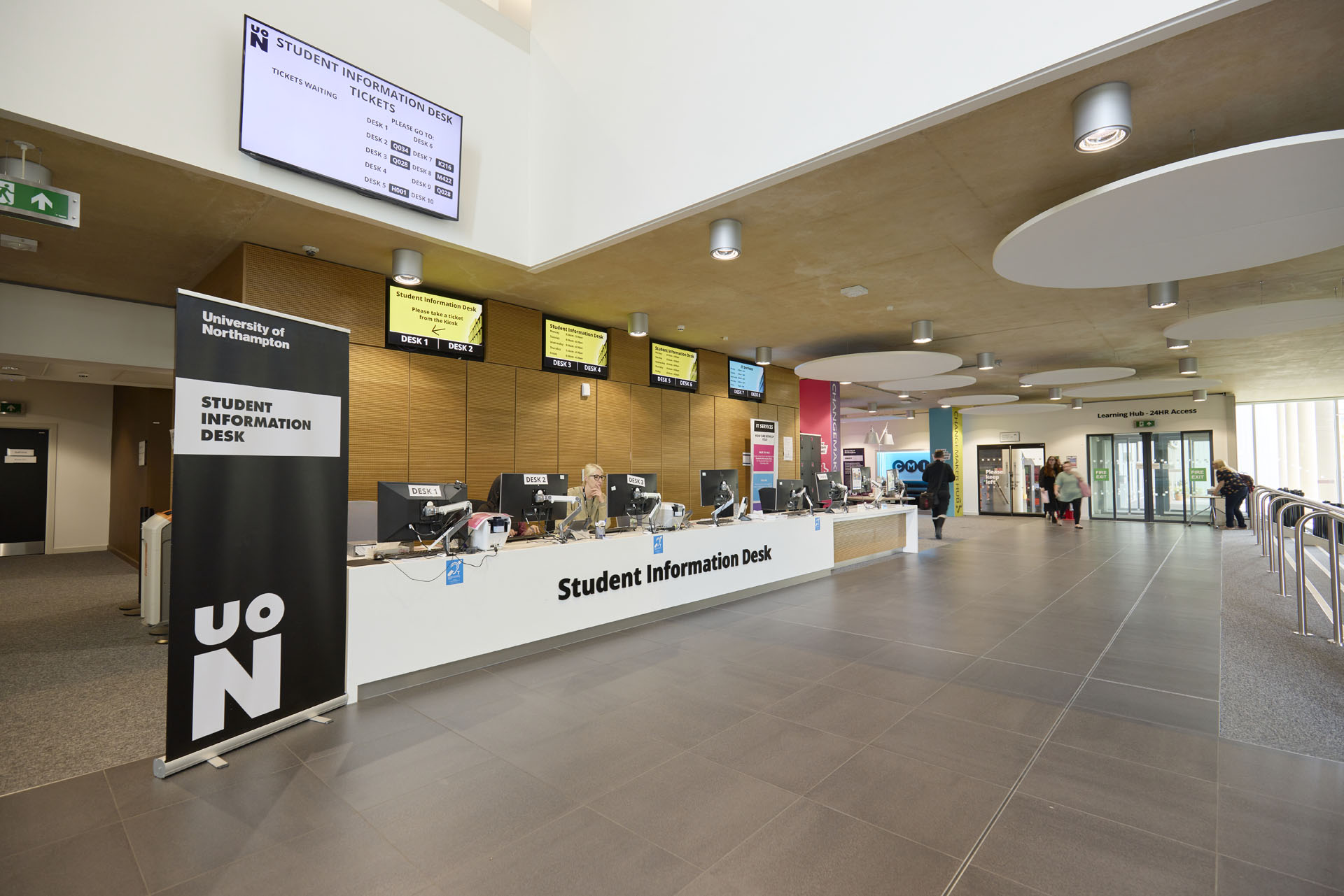 University of Northampton Student Information Desk area with digital screens, staff computers, and a sign reading