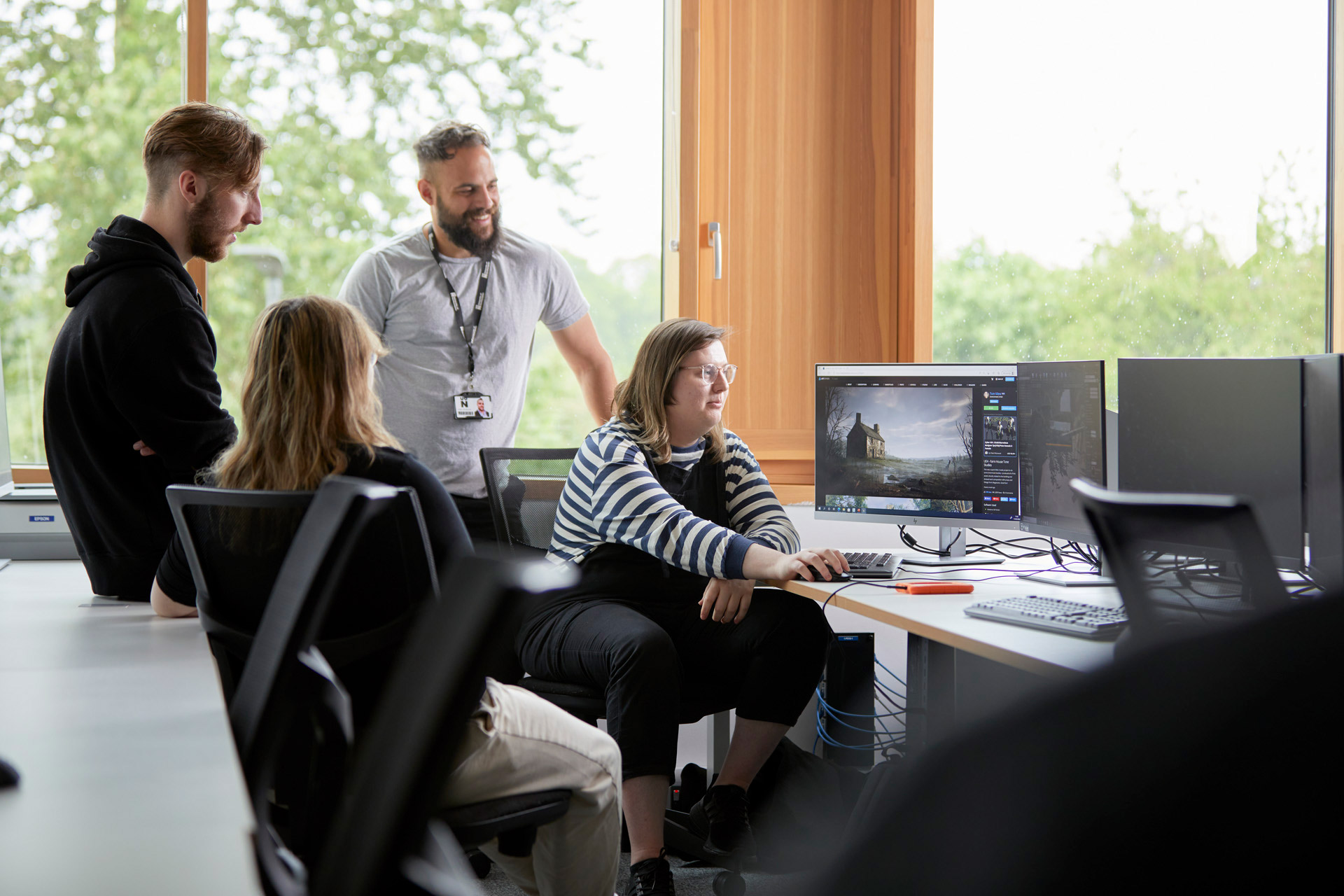 Academic and students discussing games design on two desktop screens during a tutorial