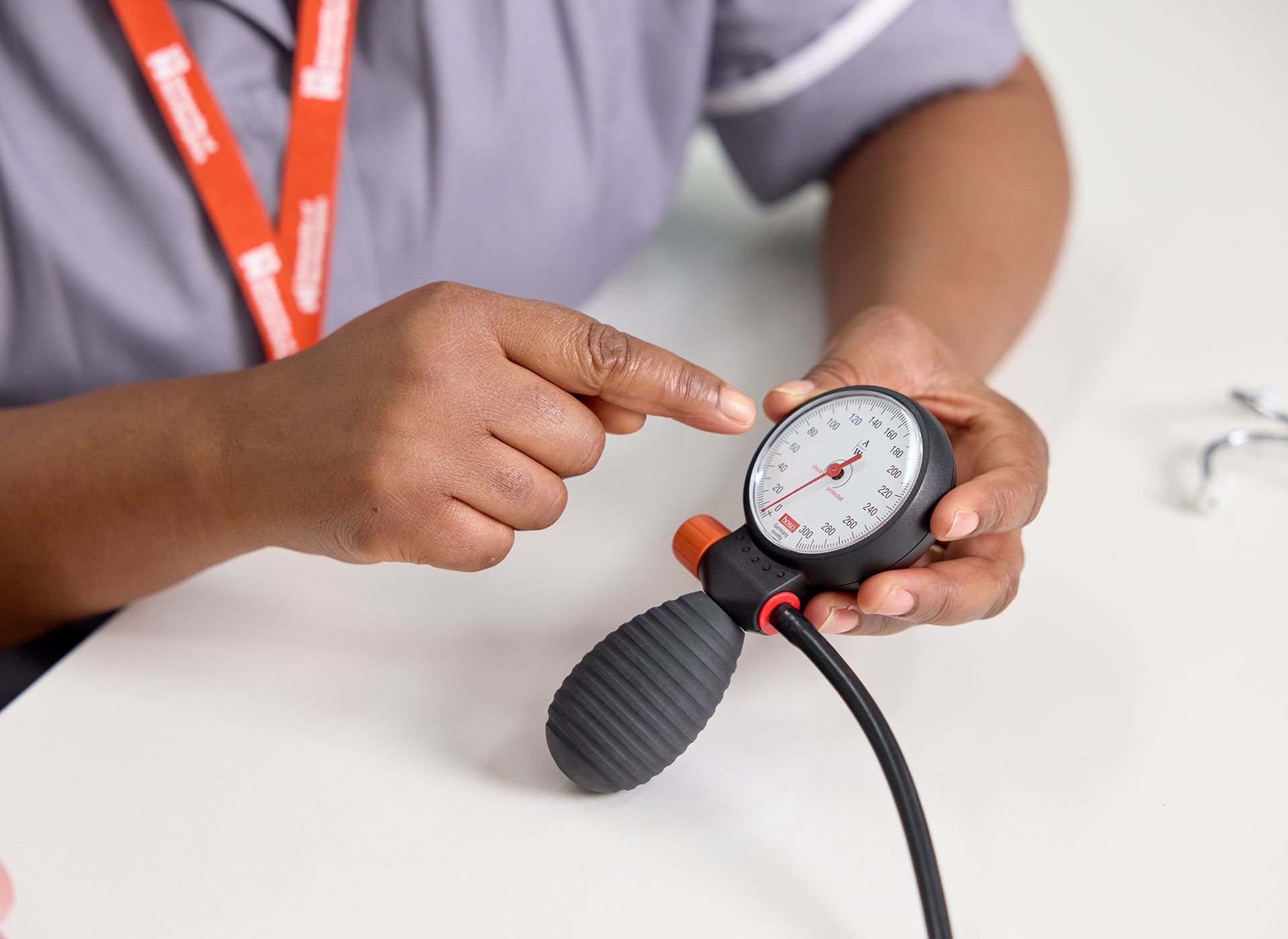 A student holding a sphygmomanometer while pointing at its gauge, indicating a blood pressure reading.