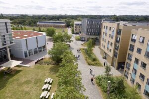 Aerial view of a Waterside campus with several buildings, green spaces, trees, pathways, and groups of people walking or standing outdoors.